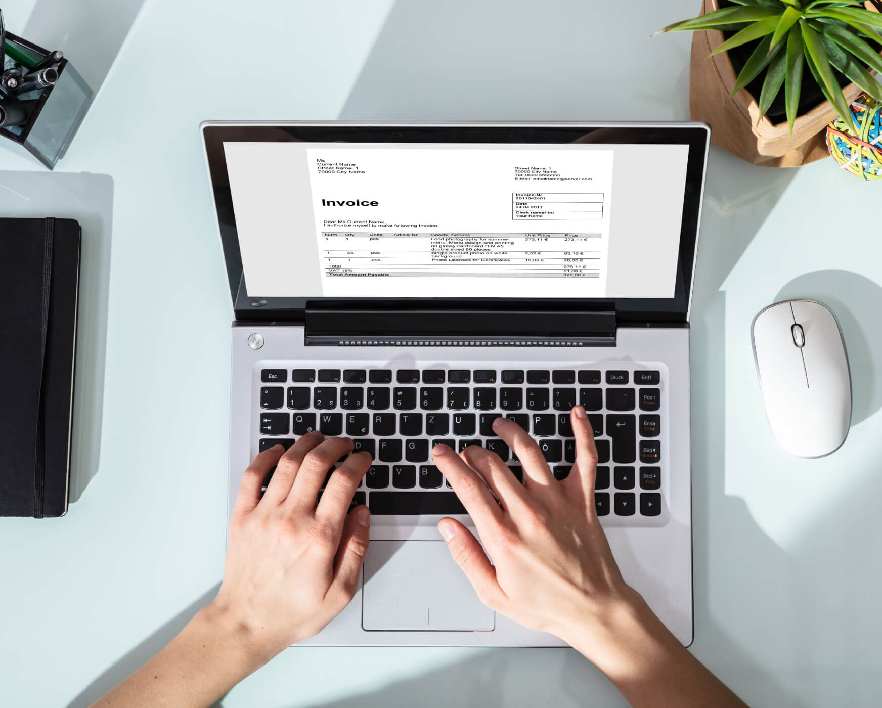 Overhead view of hands typing on a laptop with invoice on screen.