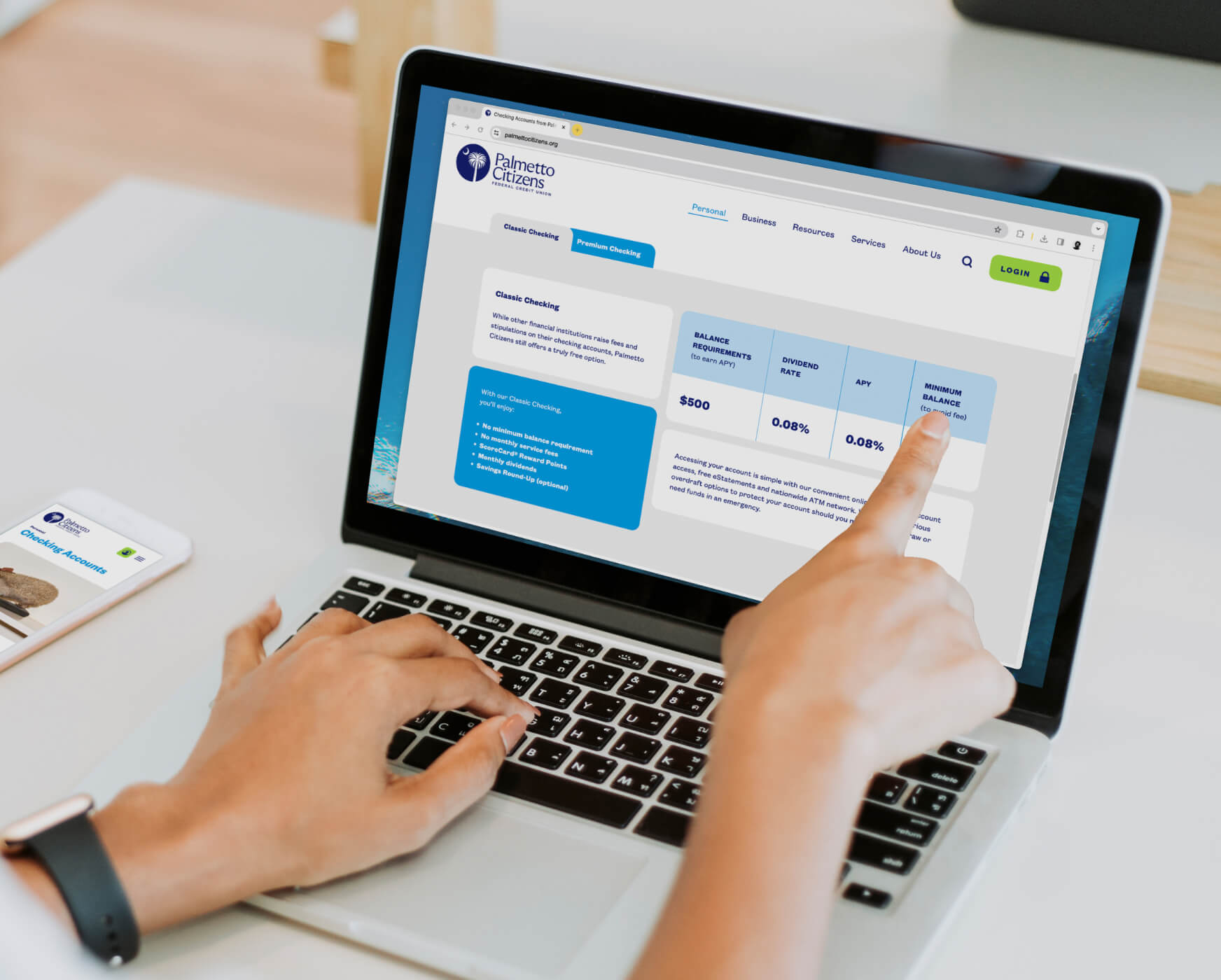 Over the shoulder view of a laptop with Palmetto Citizens loan information on screen. A hand points at the screen.