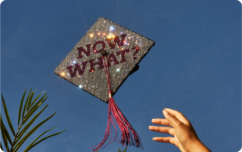 A hand throws a graduation cap in the air. The cap is bedazzled with the words Now what?